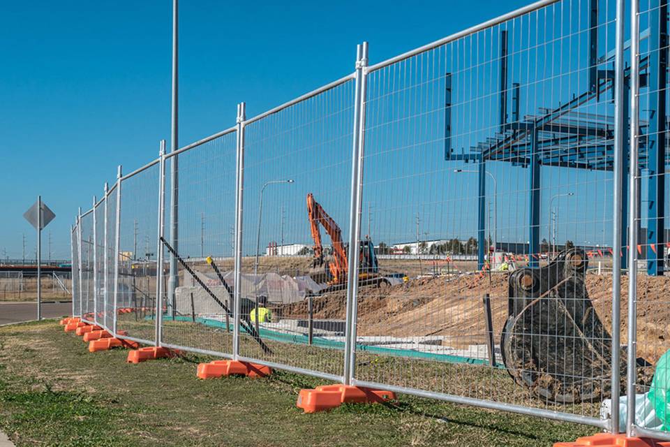 Un creuseur travaille sur le chantier de construction entouré d'une clôture temporaire australienne.