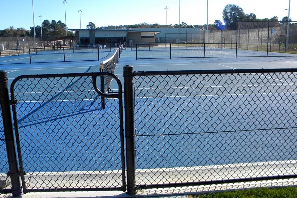 A badminton net is placed in the middle of the court encircled by chain link fence.