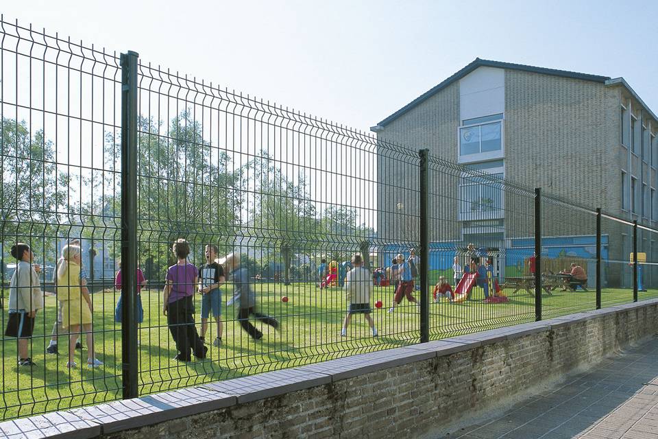 Several kids are playing in the playground encircled by curvy welded fence.
