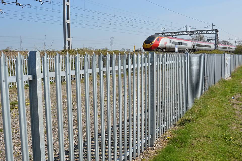 A train is running on the railway track enclosed by palisade fencing.